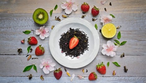 une assiette avec du thé, des fruits autour et des fleurs